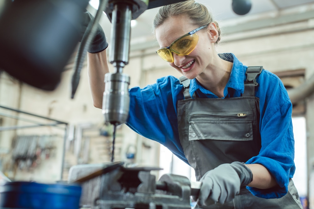 Woman worker in metal workshop using pedestal drill